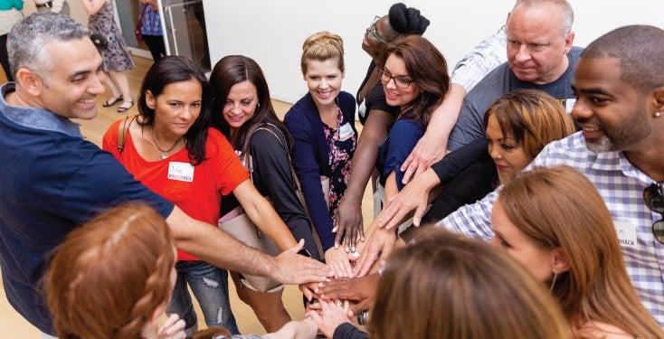 Corporate events start with a cheer, so this group of adult men and women have their hands in the middle.